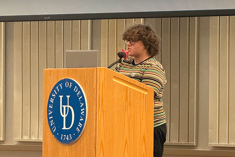 A college student delivers a speech behind a podium with a microphone.