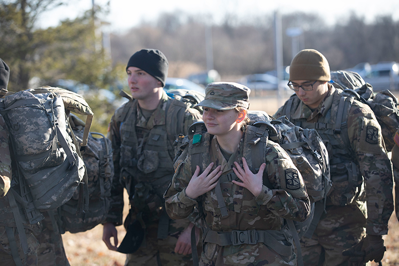 Army ROTC cadets marching in fatigues with backpacks.