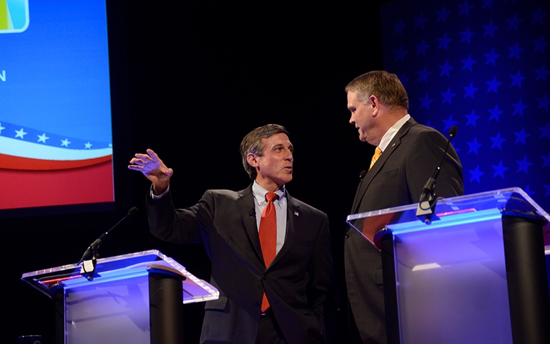 Two political candidates talk to each other while standing next to podiums on stage inside Mitchell Hall Theatre at the University of Delaware.