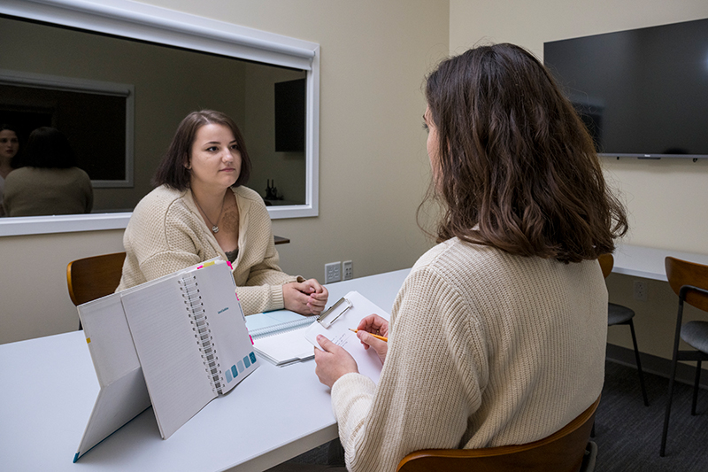 A clinician and patient sit and talk inside a private office.