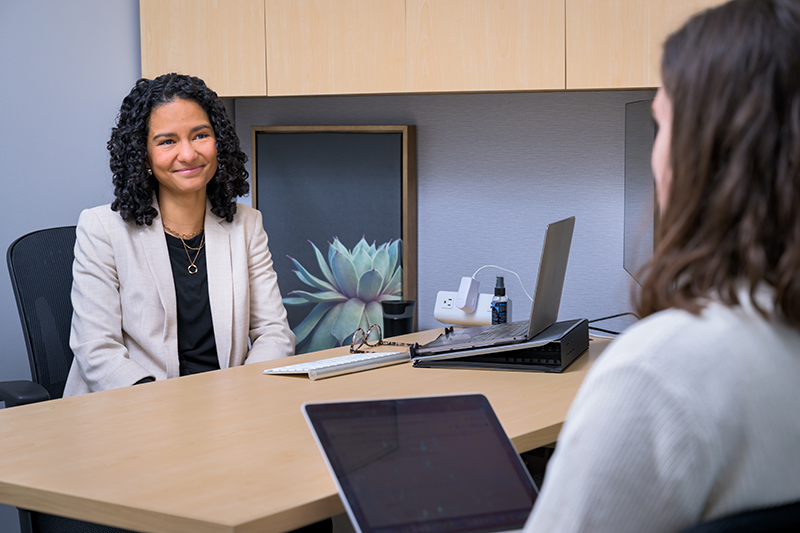 Two women meet inside an office, facing each other across a desk