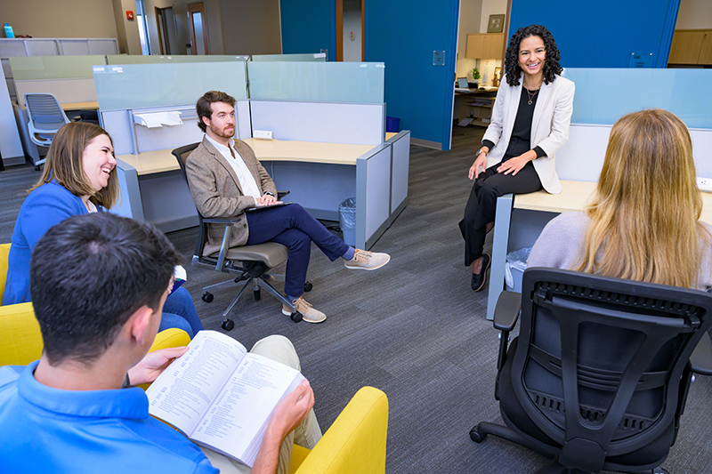 A clinical supervisor addresses four clinicians in an office.