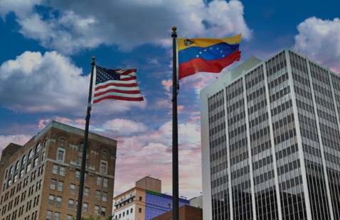 Side by side U.S. and Venezuelan flags between city buildings.
