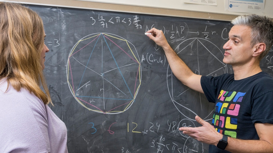 Graduate student and professor doing math equation at a black board