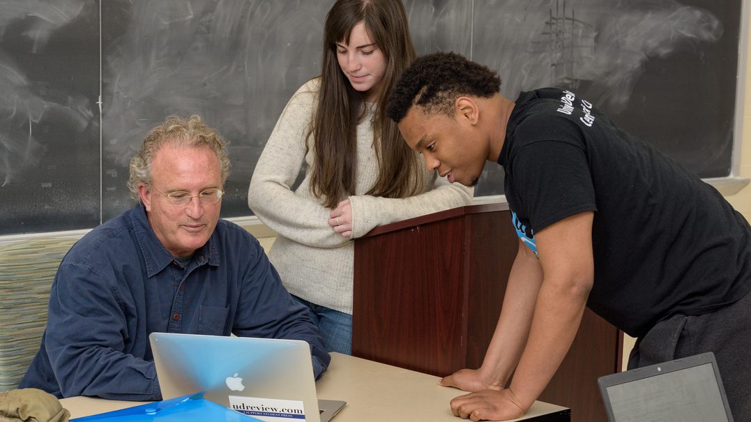 Professor and students talking over laptop
