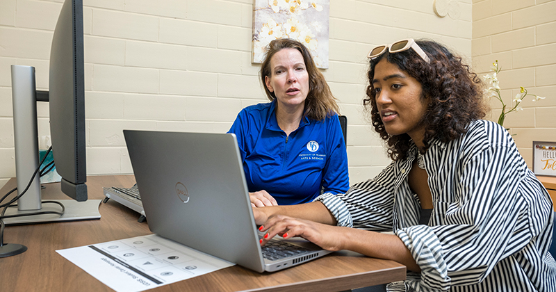 A University of Delaware College student gets help with an advisor on her project as she types on her laptop.