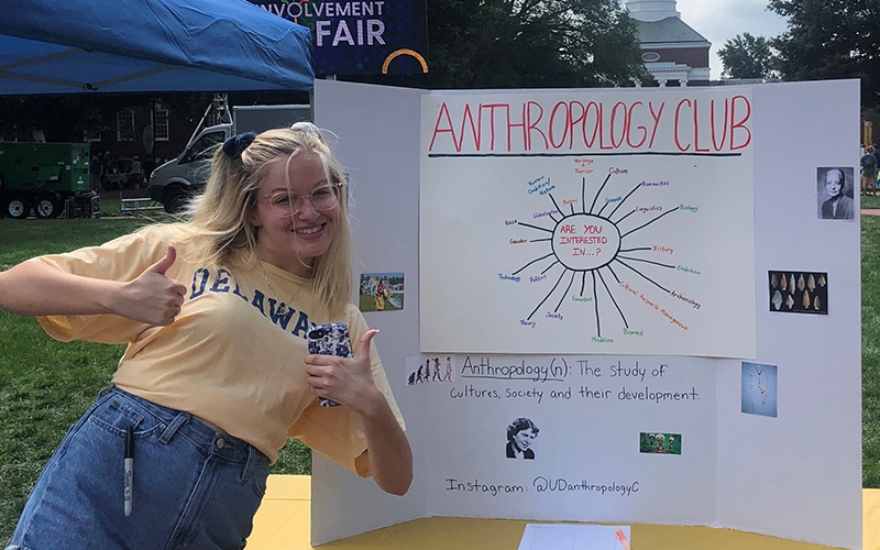 A University of Delaware student attending UD's fall involvement fair stands next to a sign for the Anthropology Club.