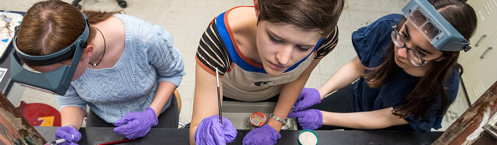 Art conservation students hold tools and work on preserving artwork