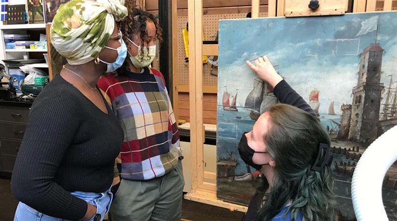 Teaching assistant and two students discussing painting conservation.
