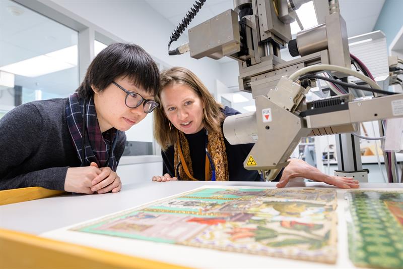 Student and faculty examining an old Victorian scrapbook with a microscope