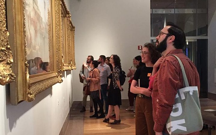 Art history students in a museum view artwork on a wall.