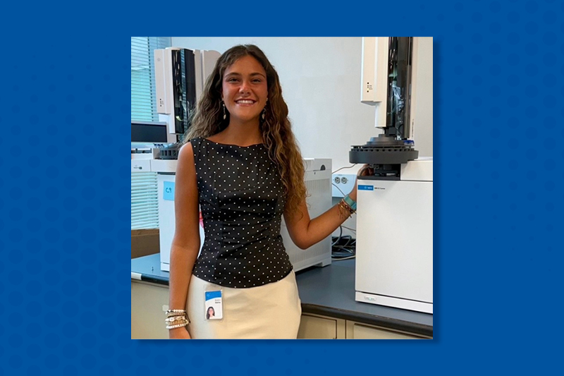 Smiling college student standing in front of office equipment while working at her summer internship.