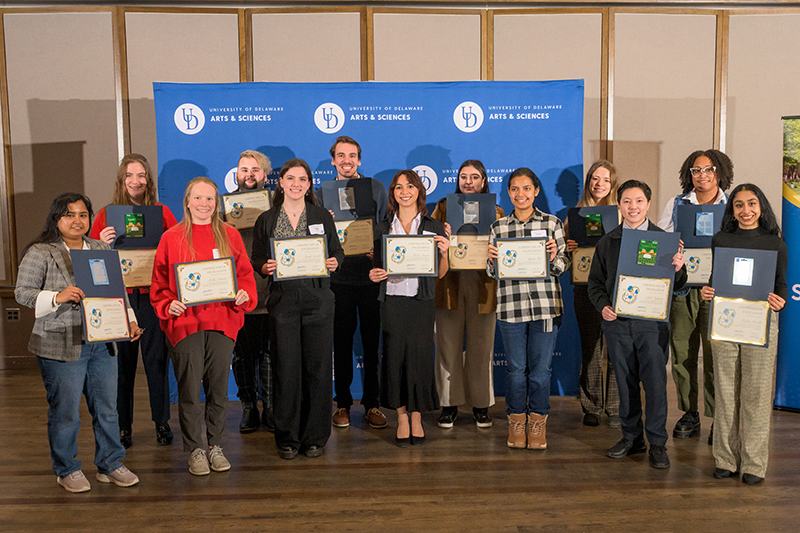 Smiling college students holding award certificates gather for a group photo during a college event.