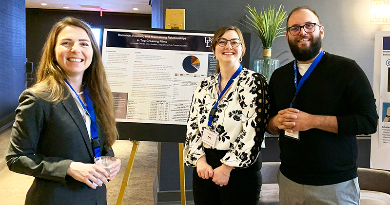Three University of Delaware graduate students attending a conference in Philadelphia stand next to easels with poster presentations of their research.