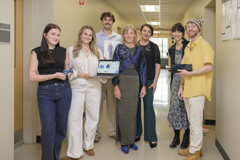 UD president Laura Carlson models her new dress while standing in the center of a group of six Fashion & Apparel students and faculty.