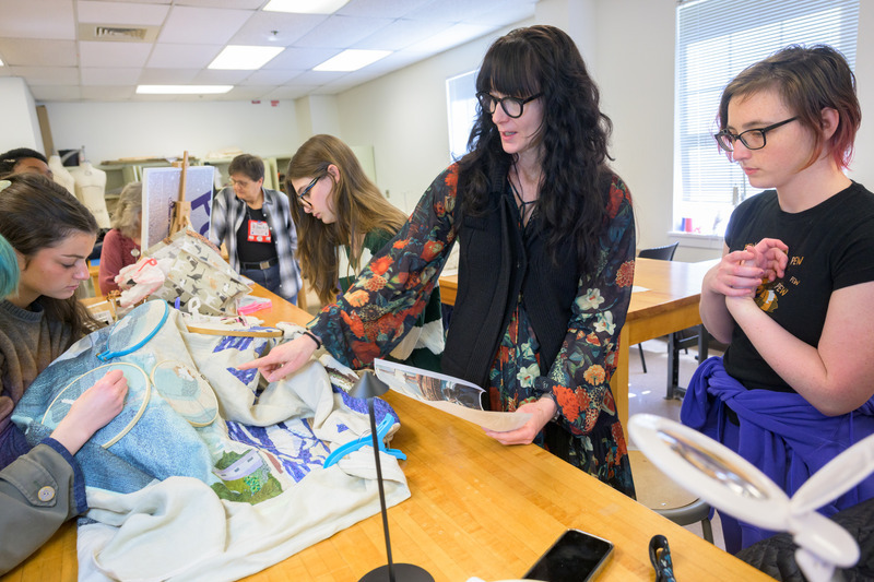 A group of students and faculty work inside a studio stitching tapestry panels.