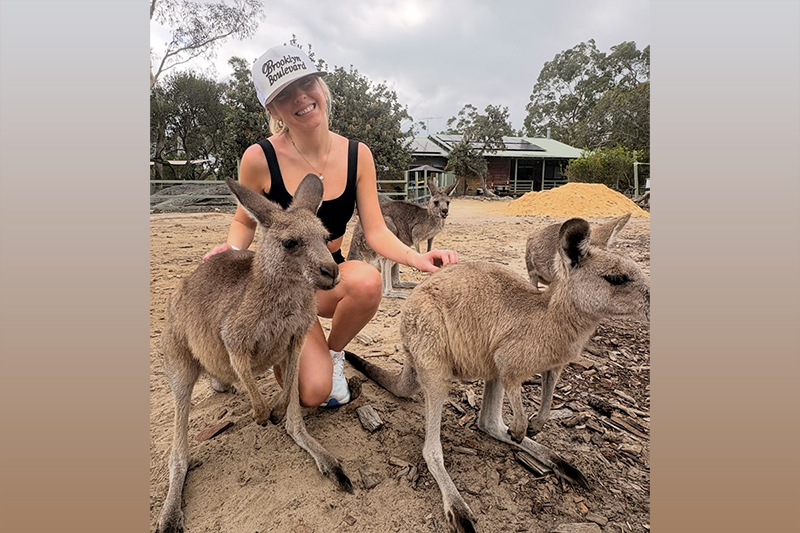 A college student kneeling with three kangaroos.