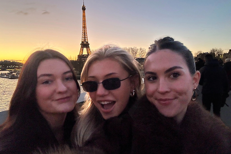 Three college students in Paris, France, in front of the Eiffel Tower at sunset.