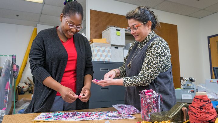 UD research assistant Diadem Abayode and Kelly Cobb, associate professor of fashion and apparel studies, arrange recycled textiles onto a backing material before feeding them through a felting machine