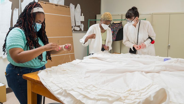 Sewing the tiers of ruffles onto the reproduction wedding gown are students Kayla Brown and Maya Bordrick and instructor Katya Roelse. The team used 154 yards of taffeta trim, basting and gathering it to make the ruffles.