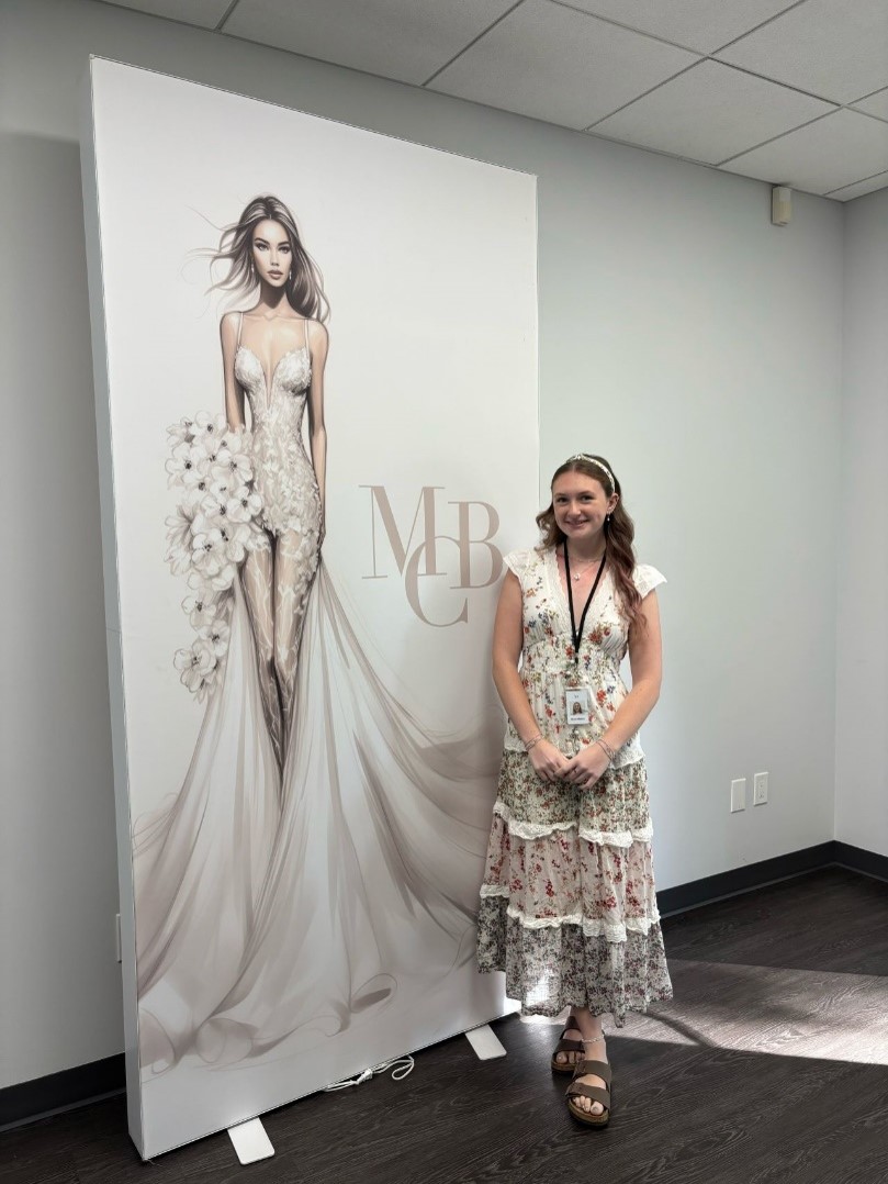Brynn Malone standing in front of a bridal gown illustration at Mon Cheri Bridals