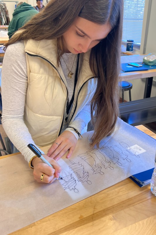 Female student with long hair leaning over table sketching on parchment paper