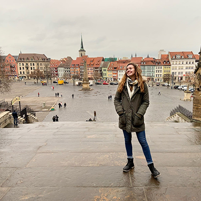 University of Delaware student Rachel Harell stands on stone steps of a historic building overlooking a city square in Leipzig, Germany.