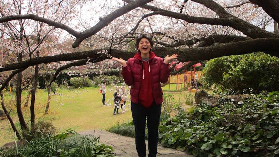 Happy female student standing under cherry blossoms