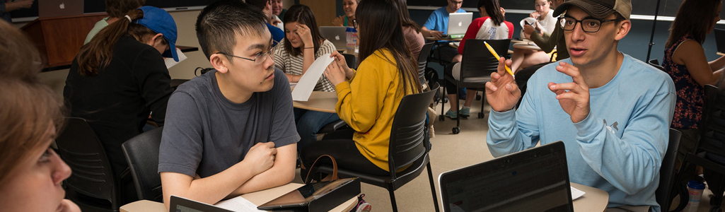 Students in classroom sit at a table as they are in a discussion.
