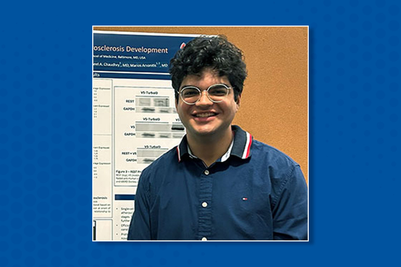 Mikul Duggal next to a poster presentation, on blue background