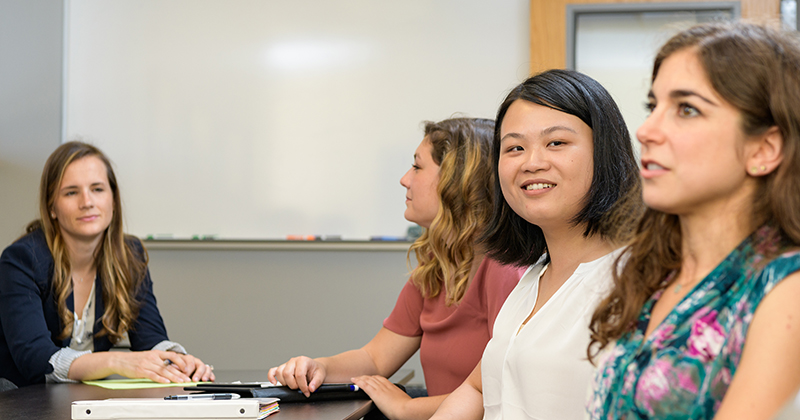 Four graduate students sit around a table in a meeting inside a conference room.