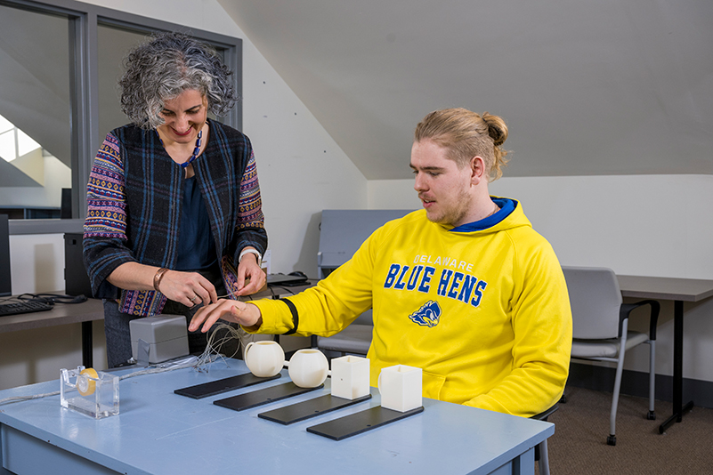 A cognitive neuroscientist applies sensors to a student's fingers during a study to track his movements.
