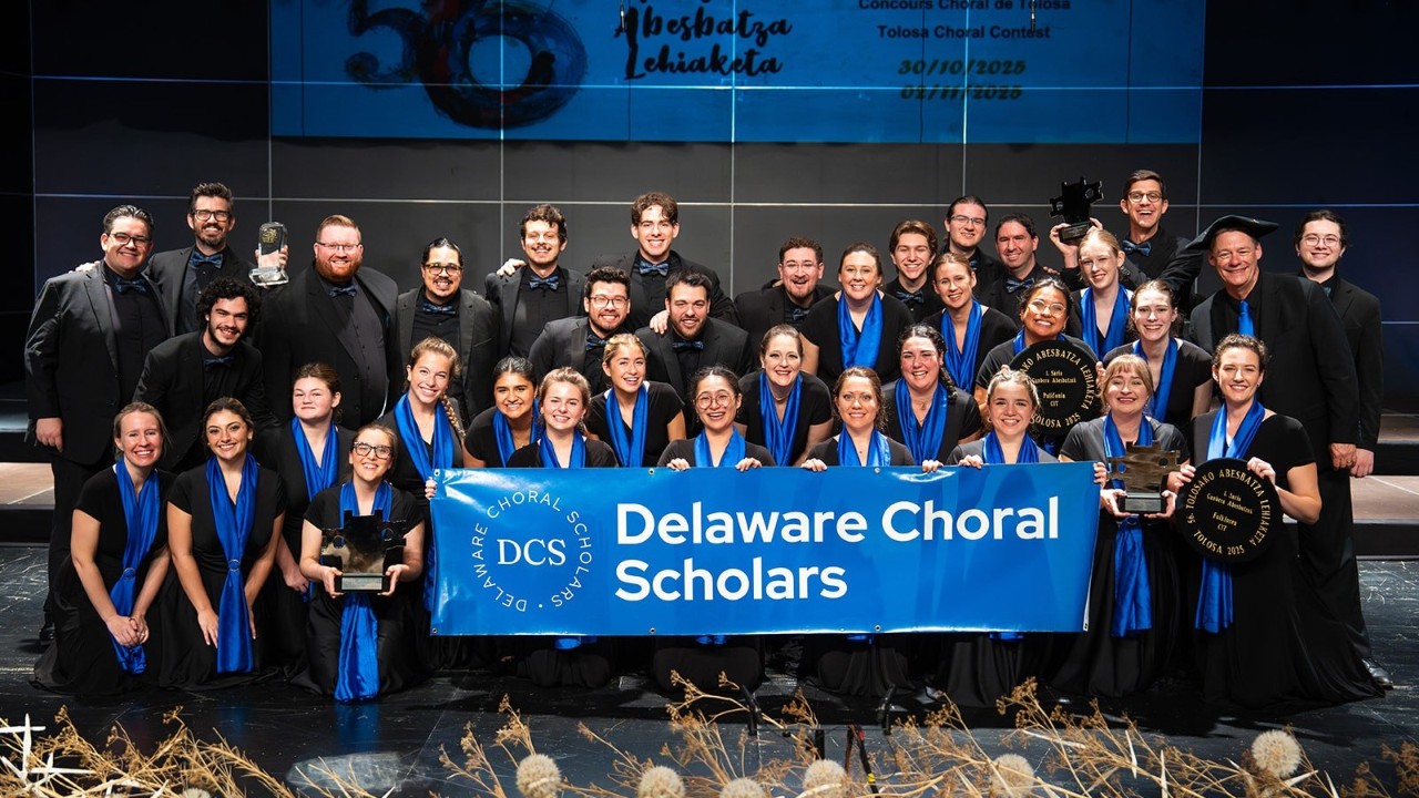 Large group of Delaware Choral Scholars holding a banner with their name on it