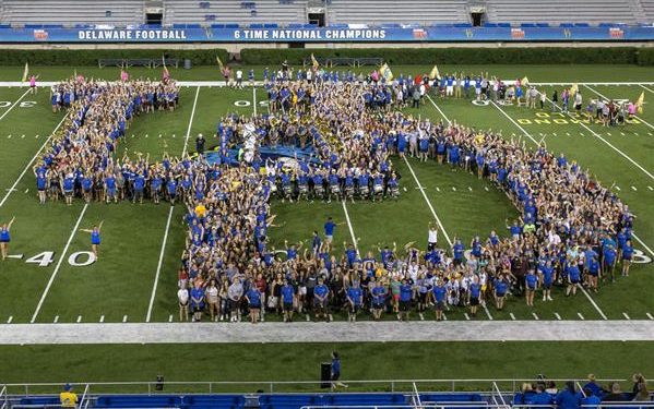 Class of 2022 fill the interlocking UD formed by the UDMB during game day. A group of people forming the letters U-D
