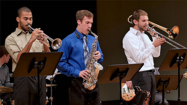 Three male students on stage playing trumpet, saxophone and trombone