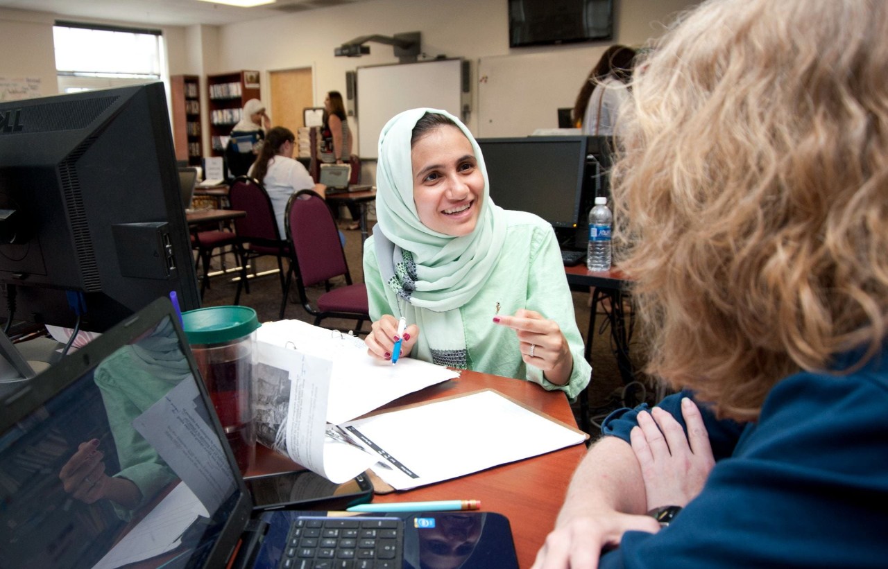 International Enlish Language Institute students in conversation with another person at a desk with computer