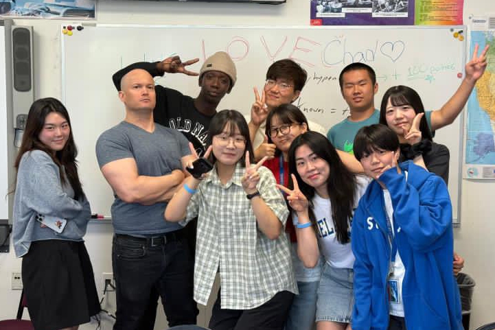 Chad Davidson, ELI instructor, is pictured with students in his classroom. The picture is fun, and goofy. The students throw up peace signs.