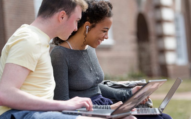 Two students sitting outside with their open laptops