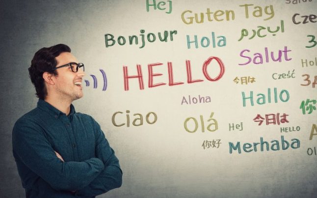 Teacher near a white board with multiple languages spelling out hello
