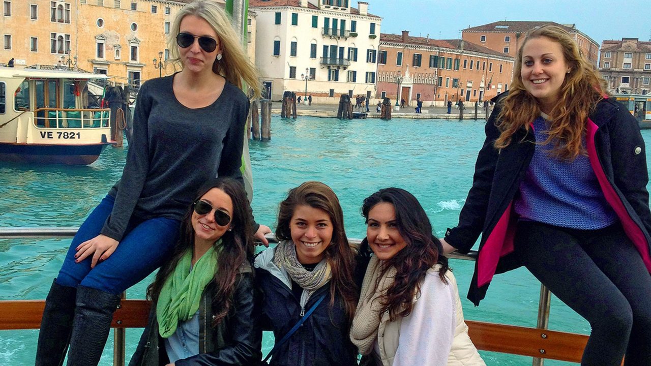 Five white female students outside in Italy near water