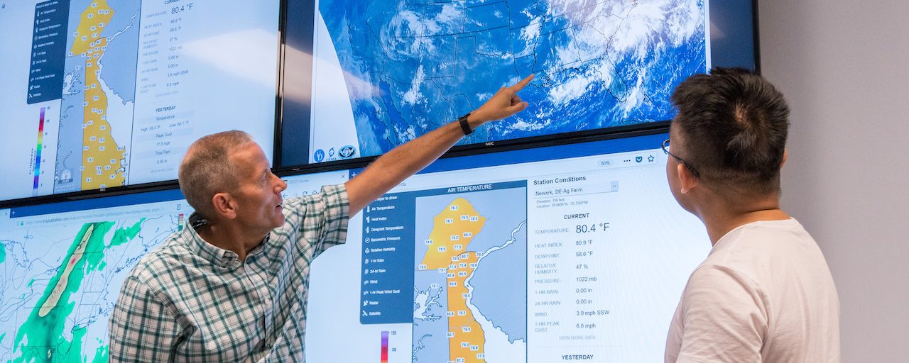 Faculty and grad student examine weather patterns on a digital display