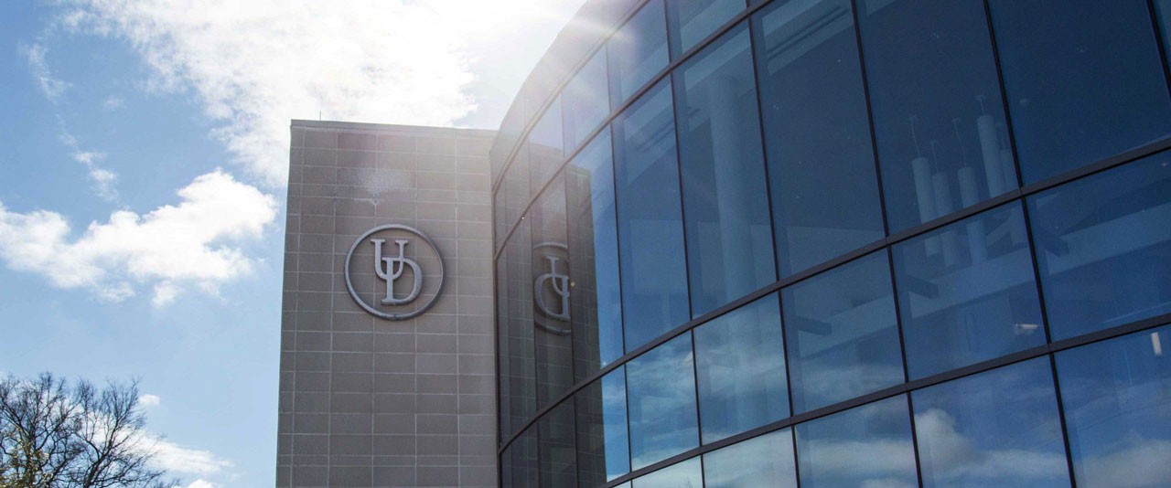 External photo of the UD Health Sciences complex atrium with the sun peaking out behind the building