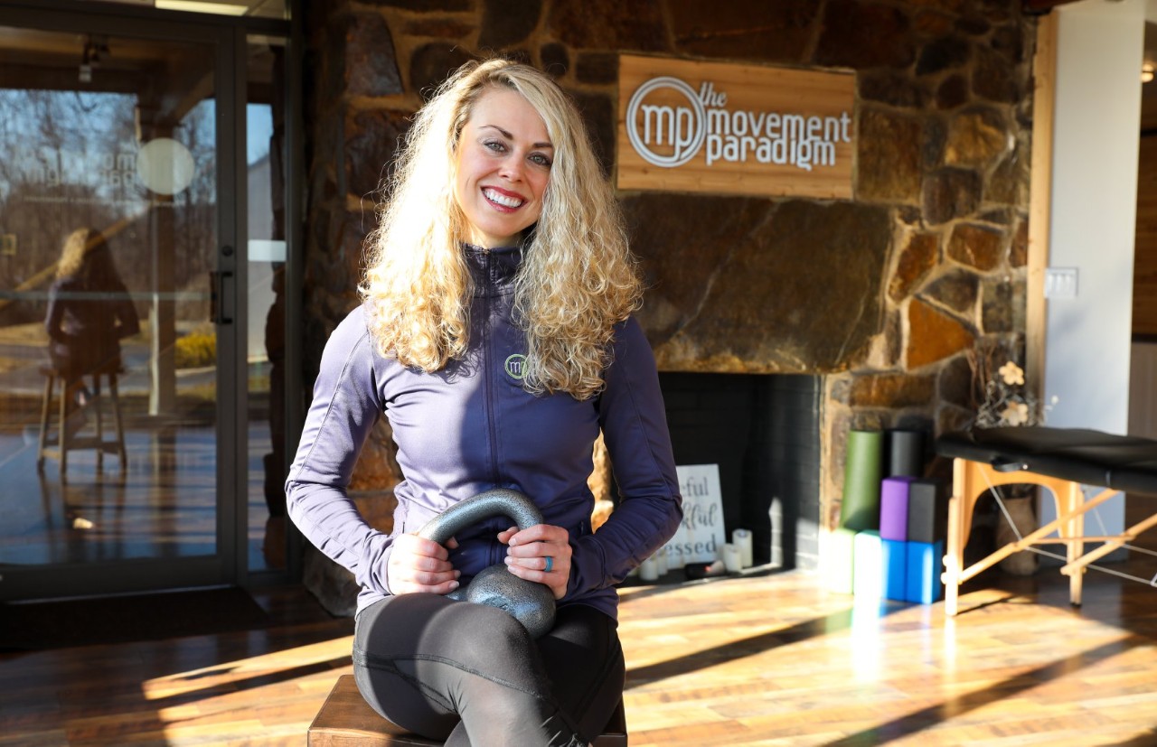 Arianne Missimer sits in a sunny workout studio holding a kettlebell