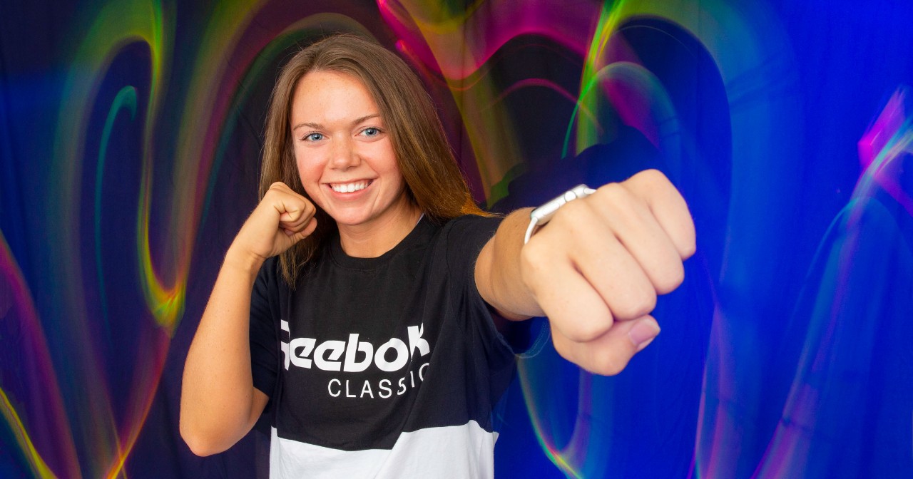 Chelsea Finch throws a punch wearing a black and white Reebok shirt against a background of neon lights
