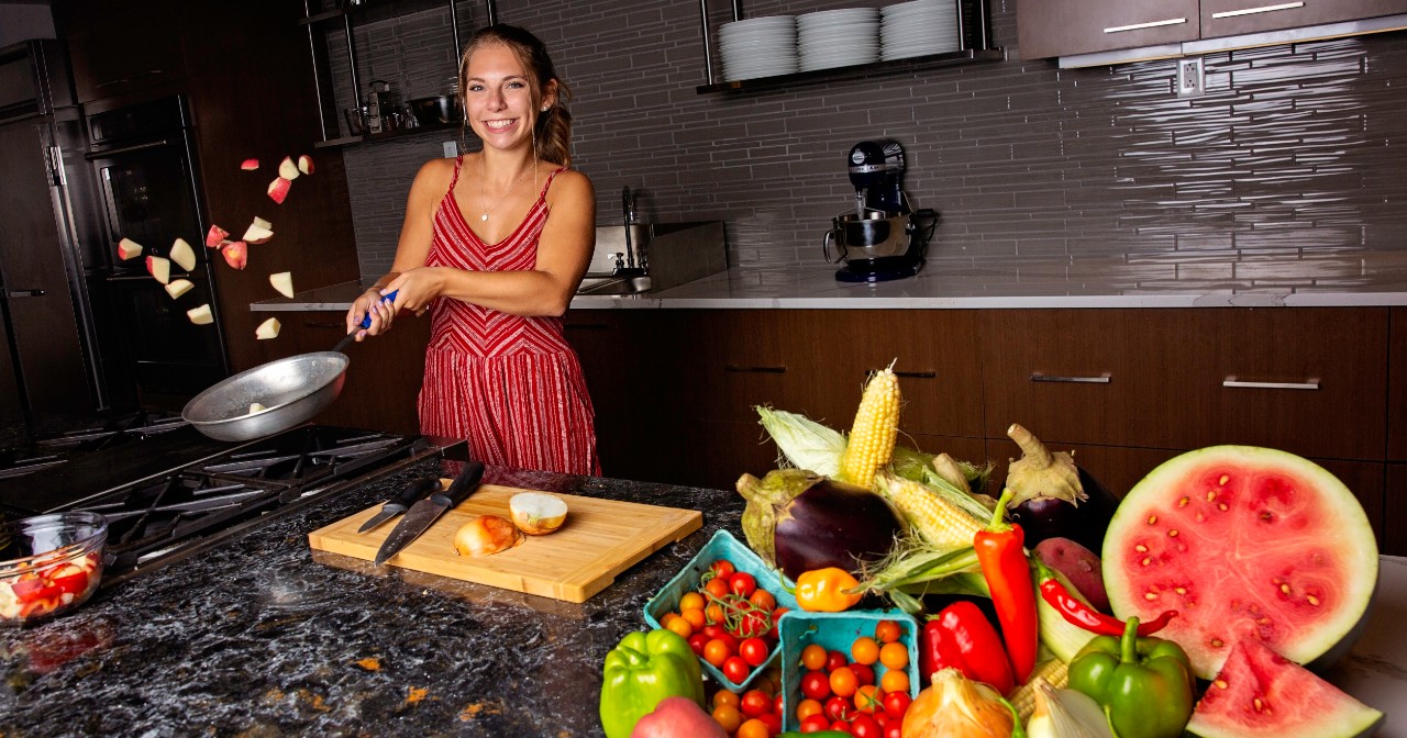 Sam Lambert tosses a pan of potatoes in the demonstration kitchen at STAR. A pile of colorful fresh fruits and vegetables are in the foreground.