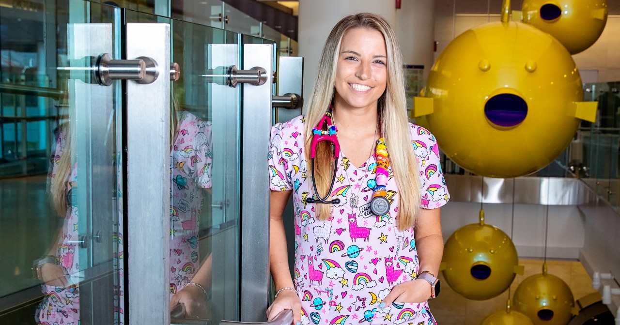Jacqueline Fabricatore wears brightly colored scrubs and stands in front of puffer fish sculptures at a children's hospital