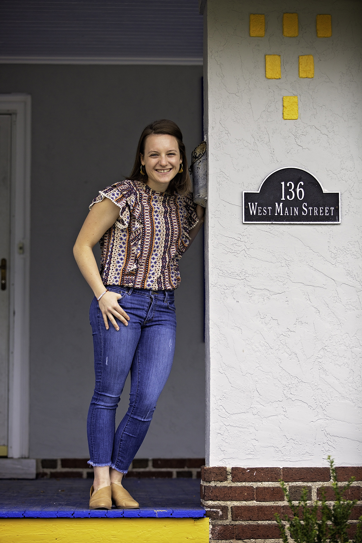 Shannon Gibbons, wearing jeans and a red and white top, leans against the entrance to Sean's House on Main Street