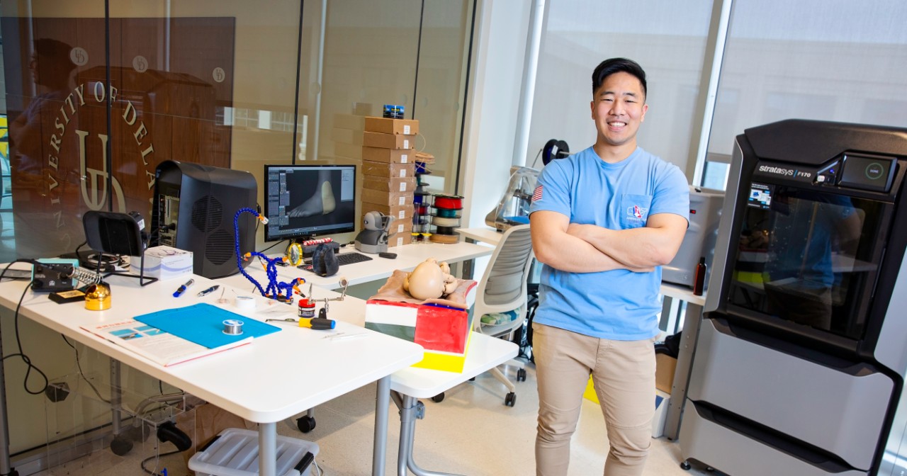Jaeah Yoo stands with arms crossed in front of his 3D printing equipment in the innovation health and design lab