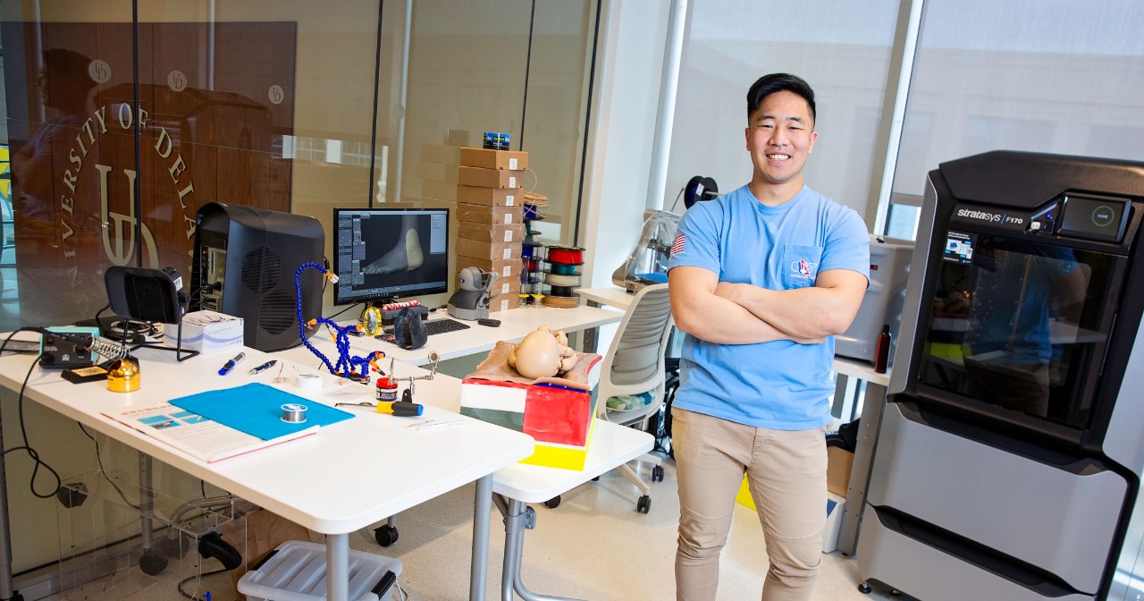 Jaeah Yoo stands with arms crossed in front of his 3D printing equipment in the innovation health and design lab