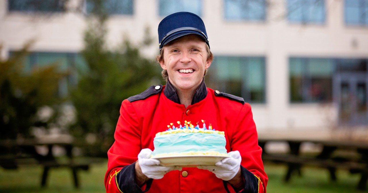 Taylor Darden wears a bellhop uniform and holds a birthday cake with flaming candles outside of STAR Campus